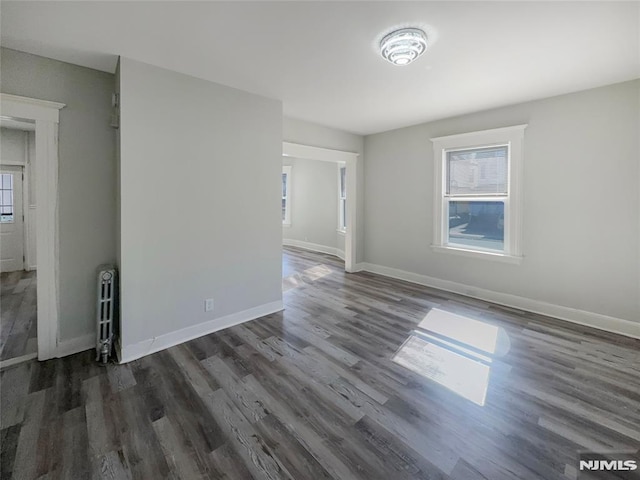 spare room featuring dark wood finished floors, radiator, a healthy amount of sunlight, and baseboards