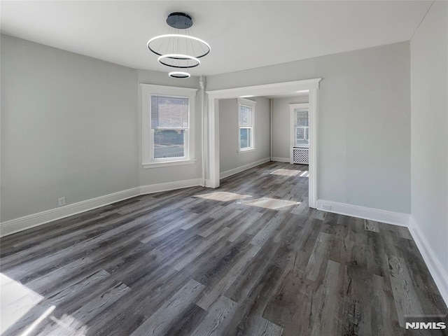 unfurnished dining area with a notable chandelier, radiator, dark wood-type flooring, and baseboards