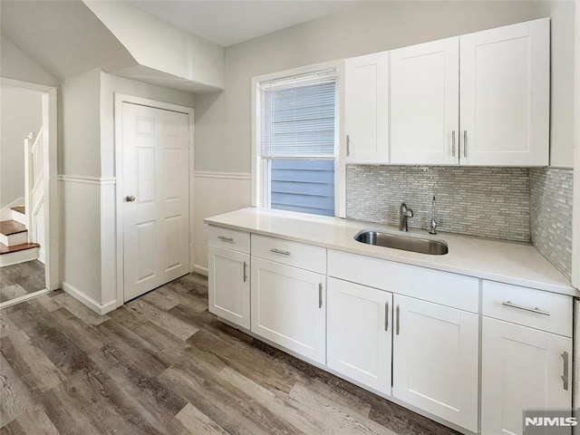 kitchen with light countertops, wainscoting, wood finished floors, white cabinetry, and a sink