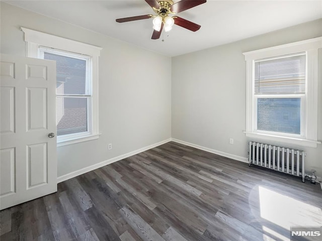 empty room with dark wood-style floors, a ceiling fan, radiator heating unit, and baseboards