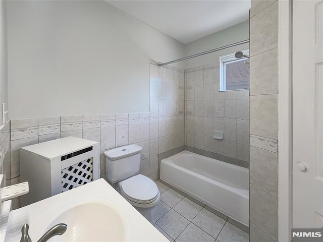 bathroom featuring tile patterned flooring, washtub / shower combination, toilet, tile walls, and a sink