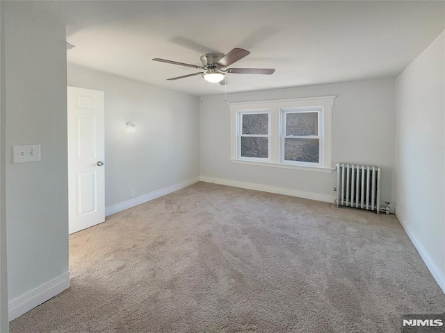 carpeted spare room with radiator, baseboards, and ceiling fan