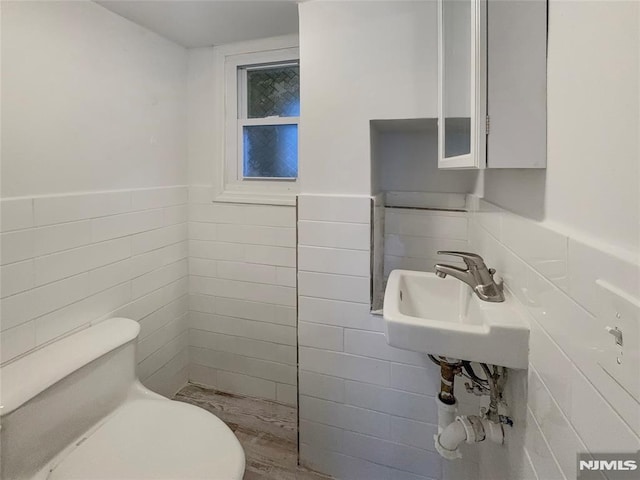 bathroom featuring a wainscoted wall, toilet, tile walls, and a sink