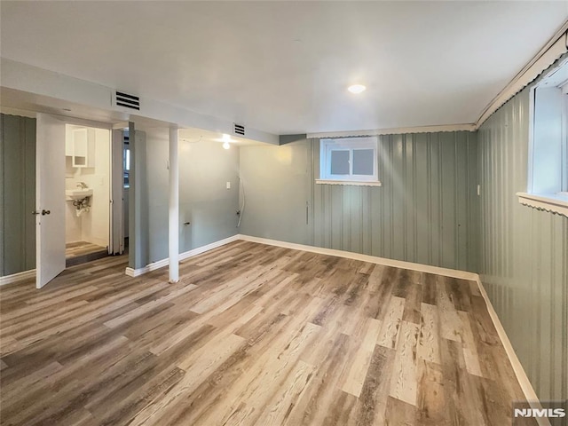 below grade area featuring visible vents, a sink, baseboards, and wood finished floors