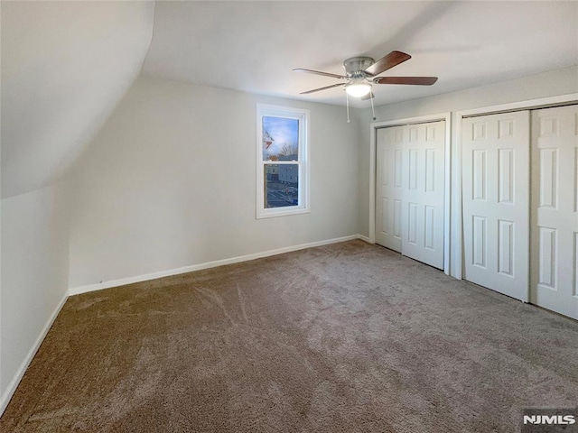 unfurnished bedroom featuring baseboards, ceiling fan, vaulted ceiling, multiple closets, and carpet flooring