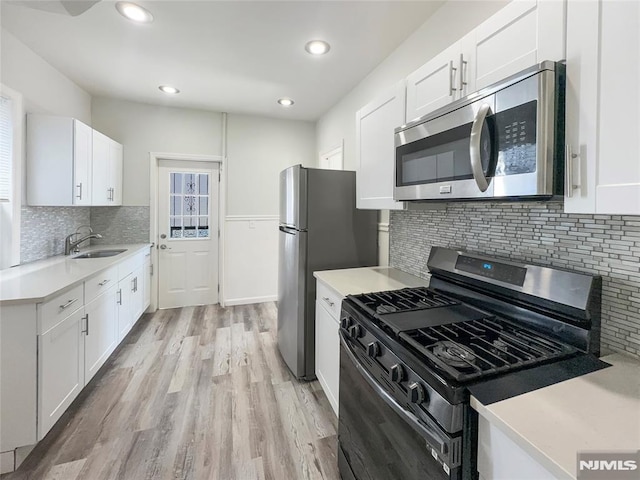 kitchen with a sink, white cabinetry, stainless steel appliances, light wood-style floors, and light countertops