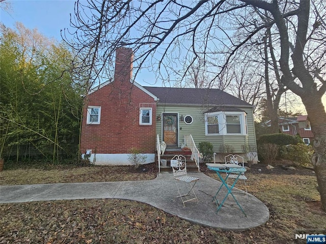 view of front of property with entry steps, a patio, brick siding, and a chimney