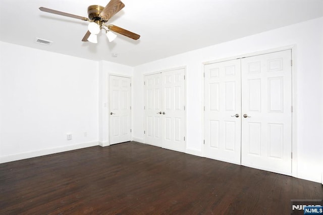 unfurnished bedroom with visible vents, baseboards, two closets, and dark wood finished floors