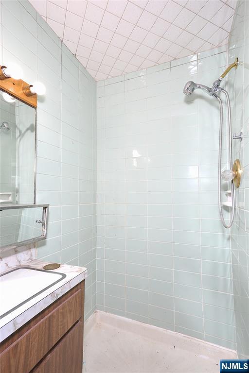 full bathroom with tile walls, vanity, and a tile shower