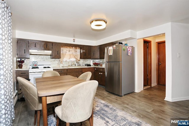 kitchen with white range with gas cooktop, under cabinet range hood, freestanding refrigerator, light countertops, and dark brown cabinets