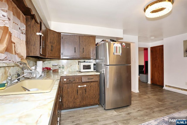 kitchen with a sink, freestanding refrigerator, light wood finished floors, white microwave, and light countertops