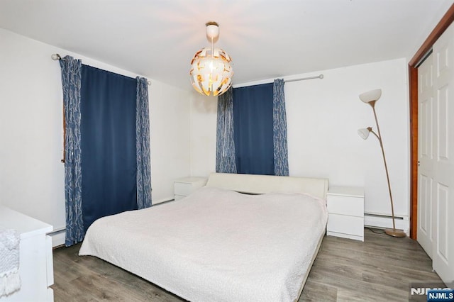 bedroom with a baseboard heating unit, a notable chandelier, and wood finished floors