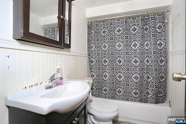 bathroom featuring a wainscoted wall, shower / bath combo with shower curtain, toilet, and vanity