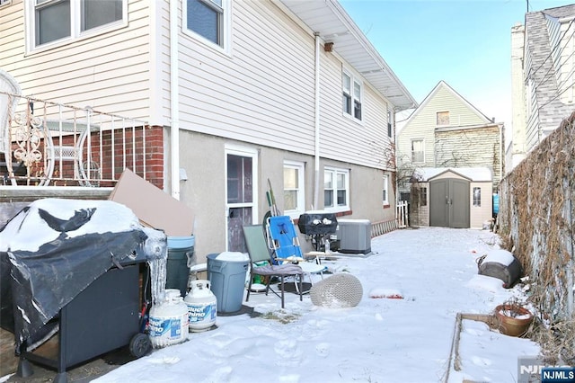 snow covered property featuring an outbuilding, a storage shed, and central AC