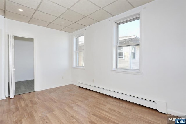 empty room with a drop ceiling, baseboards, light wood-type flooring, and baseboard heating