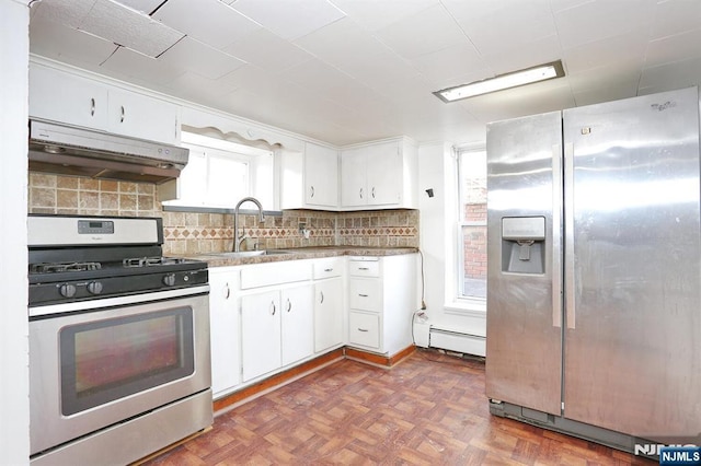 kitchen featuring a sink, under cabinet range hood, appliances with stainless steel finishes, a baseboard heating unit, and backsplash