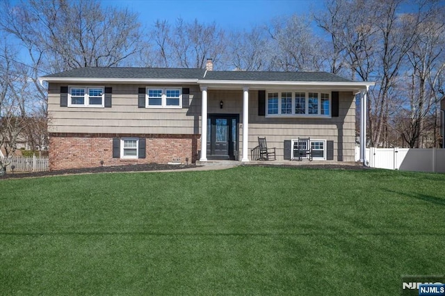 raised ranch featuring a front yard, fence, brick siding, and a chimney