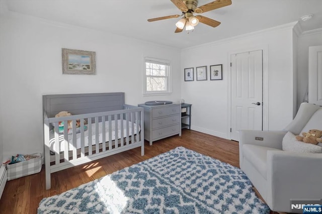 bedroom with wood finished floors, baseboards, a ceiling fan, a crib, and crown molding