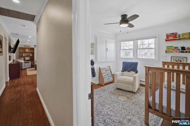 bedroom featuring dark wood-style floors, baseboards, a baseboard radiator, ornamental molding, and a crib