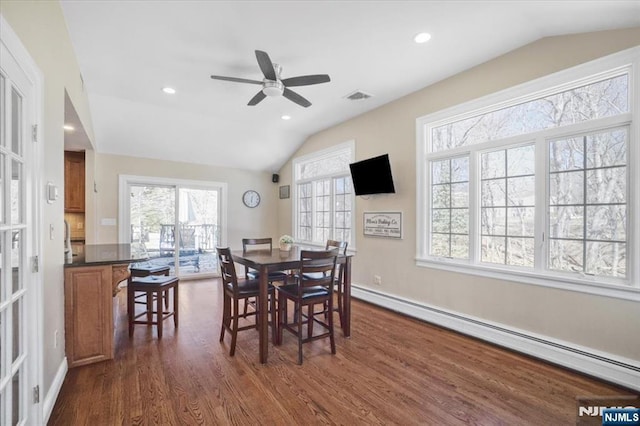 dining space with visible vents, vaulted ceiling, dark wood-type flooring, a baseboard heating unit, and a wealth of natural light