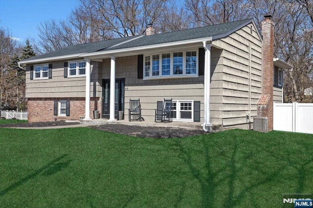 split foyer home with a front lawn, fence, brick siding, and a chimney