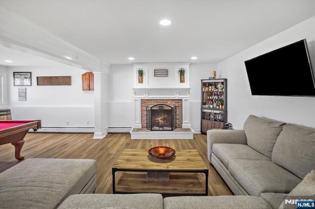 living room with a brick fireplace, a baseboard heating unit, recessed lighting, wood finished floors, and a baseboard radiator