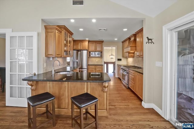 kitchen with visible vents, a peninsula, a sink, stainless steel appliances, and custom range hood