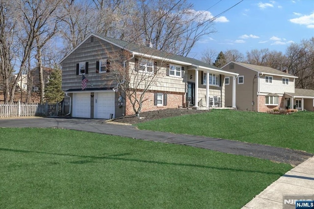 raised ranch with driveway, brick siding, a front yard, and fence