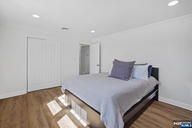 bedroom featuring crown molding, wood finished floors, visible vents, and a closet