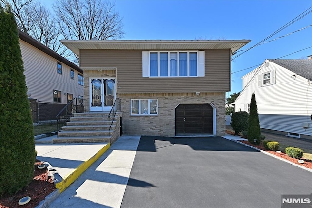 split level home with driveway, entry steps, fence, an attached garage, and brick siding