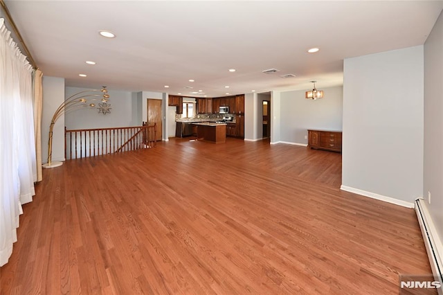 unfurnished living room featuring wood finished floors, baseboards, recessed lighting, a baseboard heating unit, and a notable chandelier