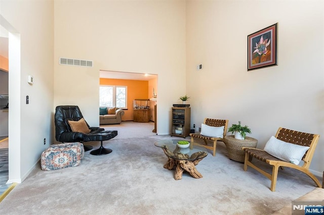 sitting room featuring visible vents, baseboards, carpet, and a towering ceiling