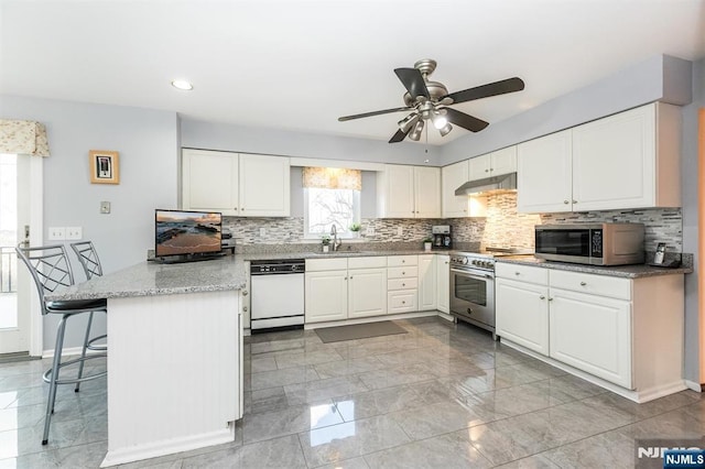 kitchen with under cabinet range hood, appliances with stainless steel finishes, a peninsula, white cabinetry, and a sink