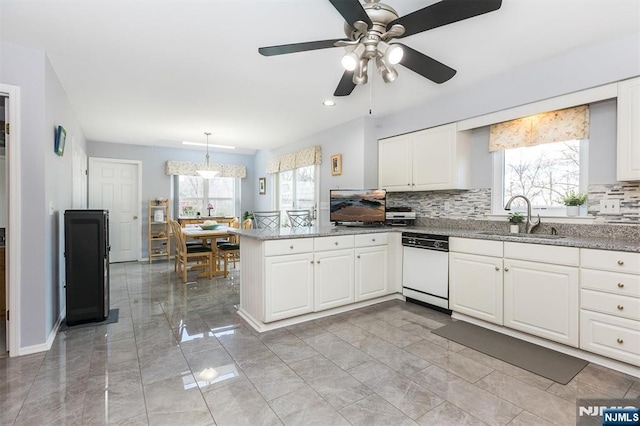 kitchen featuring backsplash, a peninsula, white dishwasher, plenty of natural light, and a sink