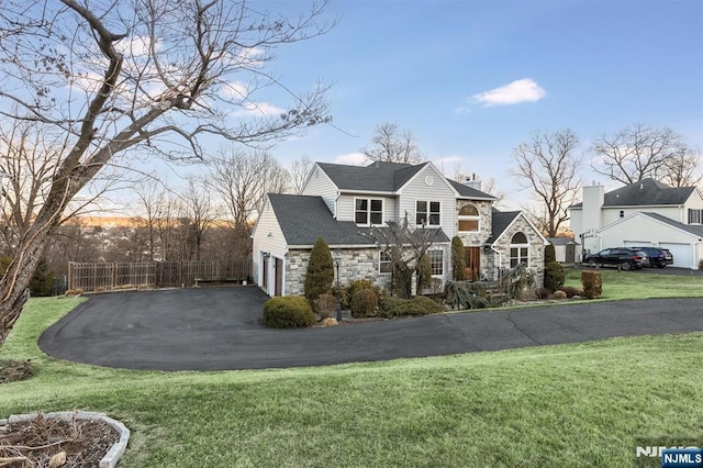 view of front facade with stone siding, driveway, a front yard, and fence