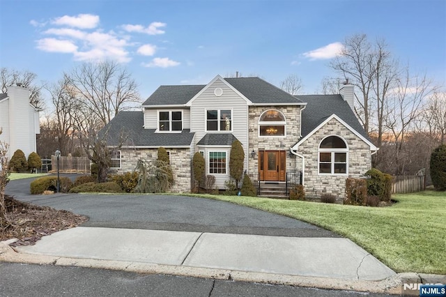 view of front of home with fence, roof with shingles, a chimney, a front lawn, and aphalt driveway