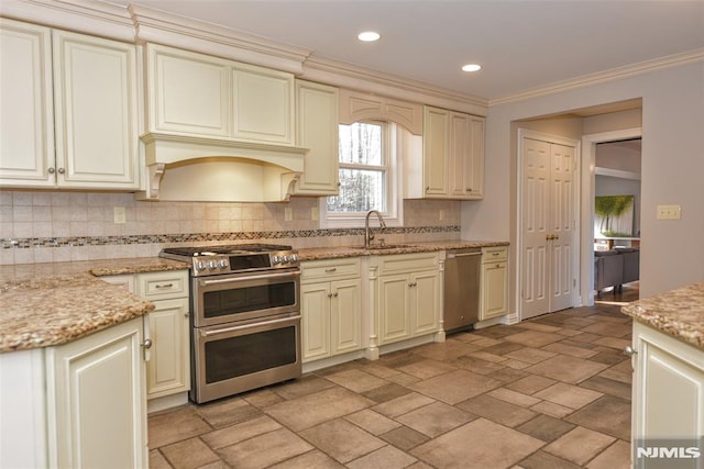 kitchen featuring tasteful backsplash, stone tile floors, appliances with stainless steel finishes, cream cabinetry, and a sink