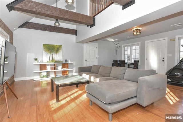 living room featuring wood finished floors, visible vents, baseboards, beam ceiling, and a towering ceiling