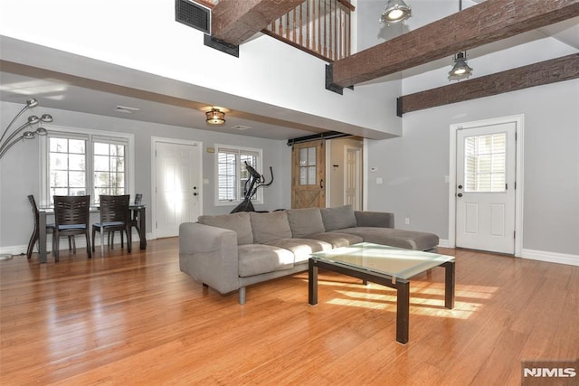 living area featuring visible vents, baseboards, a barn door, light wood-style floors, and a towering ceiling