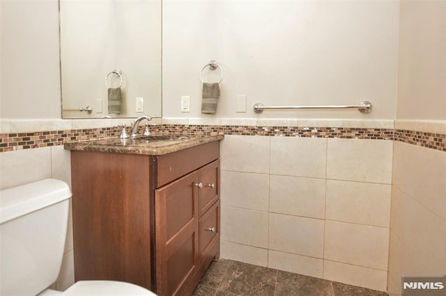 half bathroom with tile walls, wainscoting, toilet, and vanity