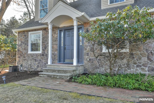 view of exterior entry featuring stone siding and a shingled roof