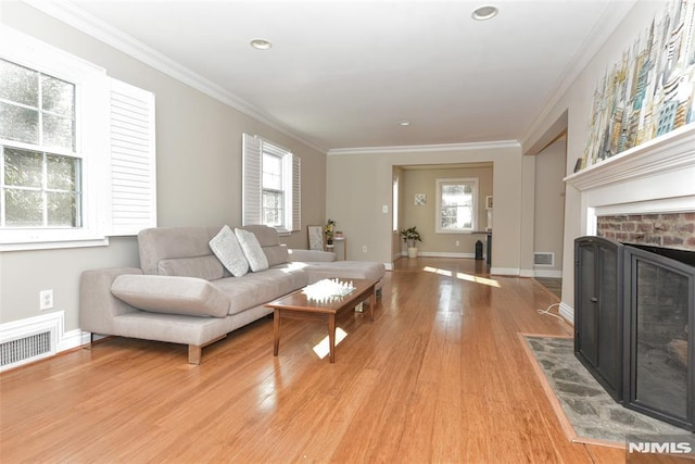 living room with a wealth of natural light, visible vents, light wood-style floors, and ornamental molding