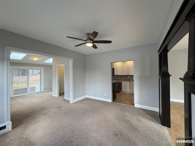 unfurnished bedroom with a ceiling fan, a skylight, light colored carpet, and baseboards