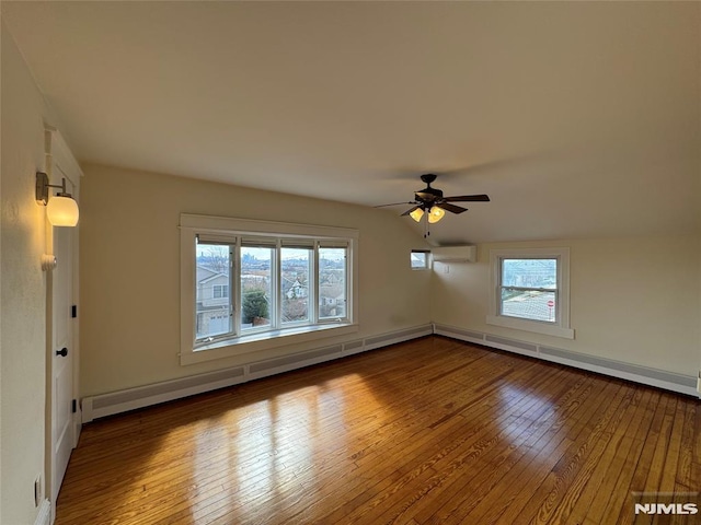 empty room featuring hardwood / wood-style flooring, a wall unit AC, baseboard heating, ceiling fan, and vaulted ceiling