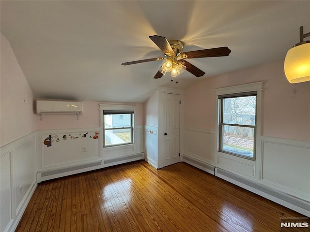 interior space featuring a wainscoted wall, a baseboard radiator, lofted ceiling, wood-type flooring, and a wall mounted air conditioner