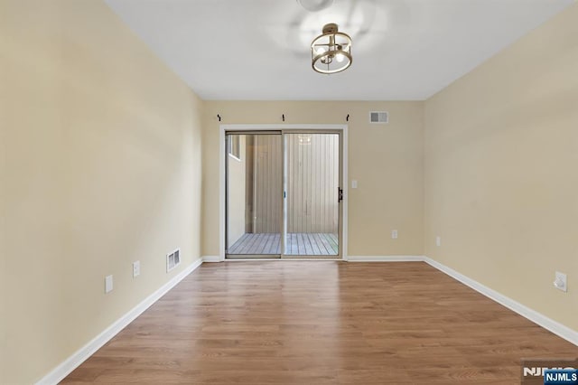 empty room with wood finished floors, visible vents, and baseboards