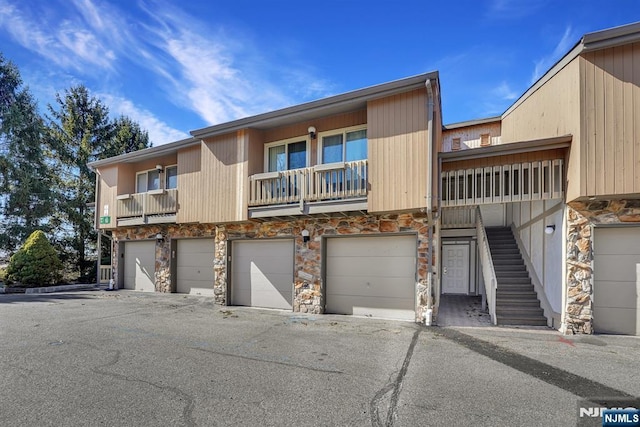 townhome / multi-family property with stone siding, an attached garage, and stairs