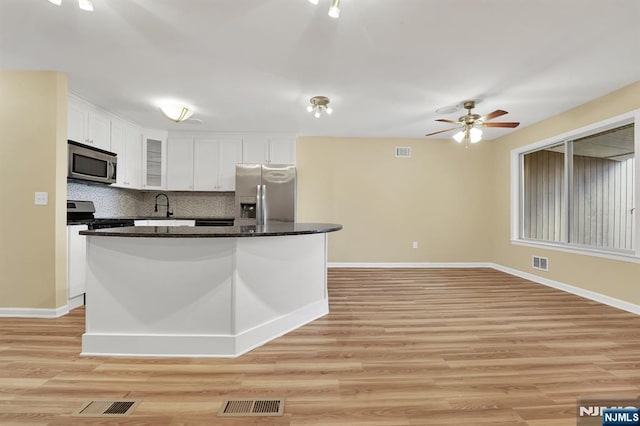 kitchen featuring a sink, backsplash, white cabinetry, appliances with stainless steel finishes, and light wood finished floors