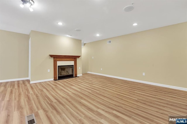 unfurnished living room featuring light wood-type flooring, visible vents, a fireplace with flush hearth, and baseboards