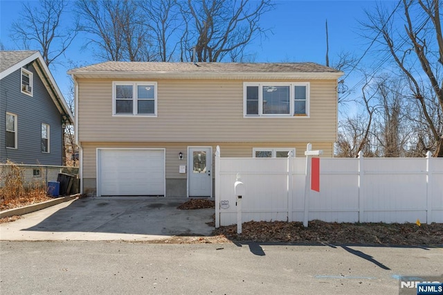 colonial-style house featuring a fenced front yard, concrete driveway, and an attached garage